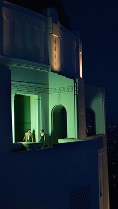 two people are sitting on the roof of a building at night with green light from below