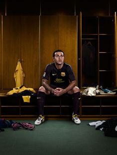 a man sitting on top of a wooden bench in a locker room next to clothes