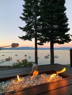 an outdoor fire pit on a deck with water and boats in the background