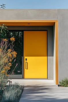 a yellow door sits in the middle of a concrete walkway next to plants and flowers