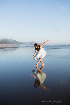 a woman standing on the beach with her arms in the air