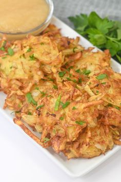 potato fritters on a white plate with dipping sauce and parsley garnish