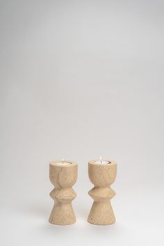 two small candles sitting next to each other on a white surface with one candle in the middle