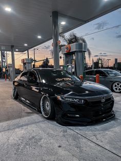 a black car is parked in front of a gas station at sunset with other cars