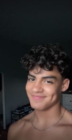 a young man with curly hair and no shirt on is smiling at the camera while wearing a chain around his neck