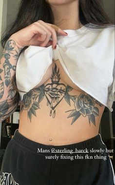 a woman with tattoos on her stomach and chest holding a piece of paper in front of her