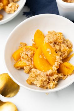 a white bowl filled with oatmeal and peaches next to spoons