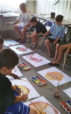 several children are sitting in chairs and painting on paper