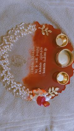 an orange plate with pearls and candles on it sitting on a white towel next to a candle holder