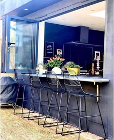 three black chairs sitting at a bar in front of an open window with potted plants on it