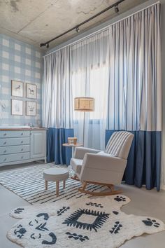 a living room with a chair and rug in front of a window that has blue curtains on the windowsill