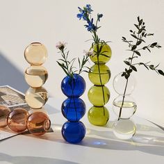 three different colored vases with flowers in them on a table next to a magazine