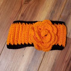 an orange and black crocheted headband with a flower on the side sitting on a wooden floor