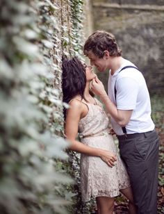 two people standing next to each other in front of a brick wall with ivy growing on it