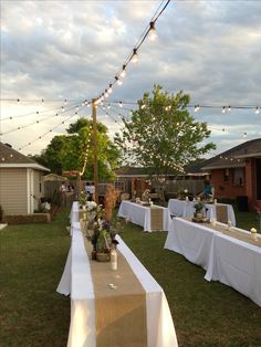 a long table set up outside with white linens and lights strung over the tables