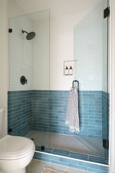 a white toilet sitting next to a walk in shower under a bathroom mirror with blue tiles on the walls