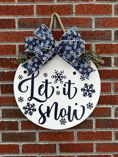 a sign that says let it snow hanging on the side of a brick wall with a bow