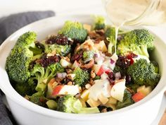 a white bowl filled with broccoli, apples and cranberry salad dressing