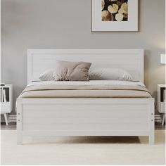 a white bed sitting in a bedroom on top of a hard wood floor next to a painting