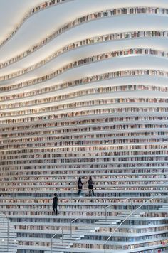 two people are standing in front of a large stack of books on the wall,