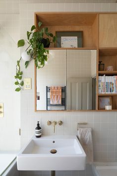 a white sink sitting under a bathroom mirror next to a wooden shelf filled with books