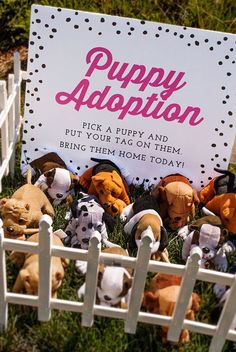 a sign that says puppy adoption with stuffed animals in the grass behind it on a white picket fence