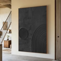 a large black piece of art hanging on the wall next to a stair case in a living room