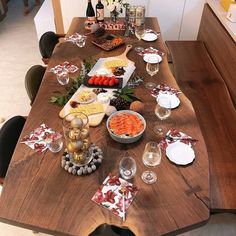 a wooden table topped with plates and bowls filled with food next to wine glasses on top of a hard wood floor