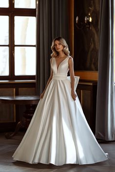 a woman in a white wedding dress standing next to a window