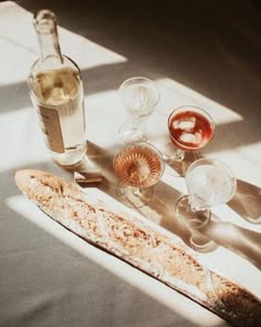 an assortment of wine glasses and bread on a table with sunlight coming through the window