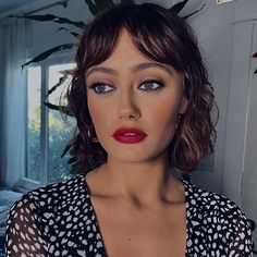 a woman with red lipstick standing in front of a plant and looking at the camera