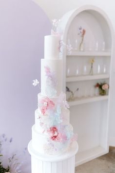 a white cake with pink and blue flowers on it sitting in front of a shelf