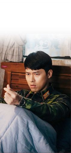 a man sitting on top of a bed next to a wooden dresser