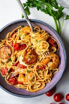 a plate of pasta with shrimp and cherry tomatoes on it, next to a fork