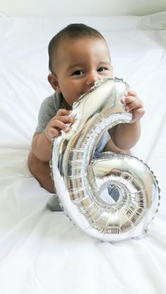 a baby sitting on the bed with a balloon in front of his face that says number six