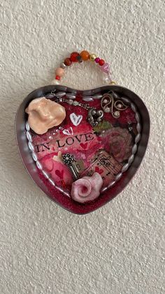 a heart shaped box hanging on the wall with beads and other things attached to it