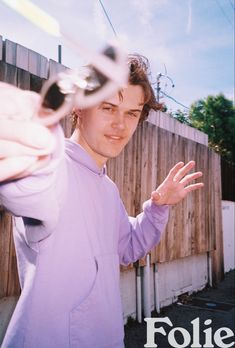 a young man is holding his hand out to the camera while standing in front of a fence