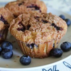 three blueberry muffins on a plate with fresh blueberries