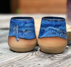 two blue and brown vases sitting on top of a wooden table next to a rock