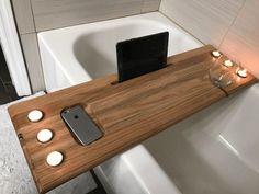 a cell phone is sitting on a wooden tray in the bathtub next to candles