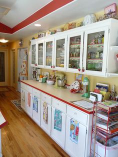 a kitchen with white cabinets and red trim on the walls, wooden floors and hard wood flooring