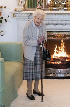 an elderly woman standing in front of a fire place holding a cane and looking at her cell phone