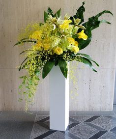 a white vase filled with yellow flowers on top of a tiled floor next to a wall