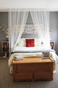 a bed with white drapes over it and a red pillow sitting on top of it