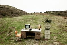 an old desk with a computer on it in the middle of a grassy hill side