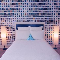 a bed with white sheets and pillows in front of a wall full of pictures on it