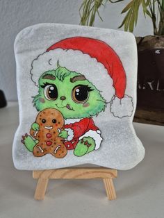 a green stuffed animal wearing a santa hat and holding a gingerbread on a wooden easel