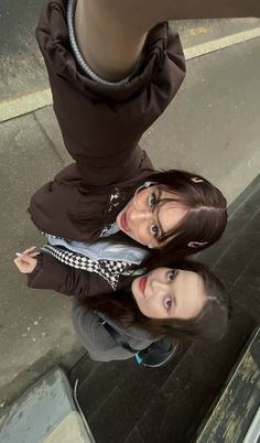 two young women standing next to each other on the side of a building, looking up at the camera