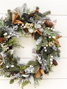 a christmas wreath hanging on the side of a white wooden wall with greenery and pine cones