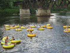 many people are floating on inflatable rafts across the water near a bridge